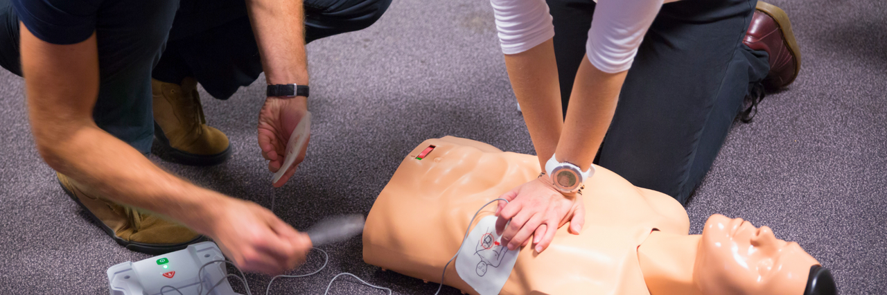Personen üben an einer Puppe die Wiederbelebung mit einem AED.